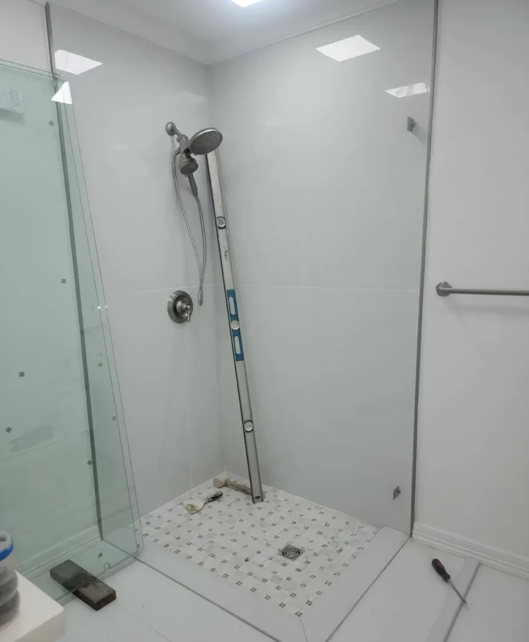 Frameless glass shower enclosure in a white-tile bathroom by USA GLASS