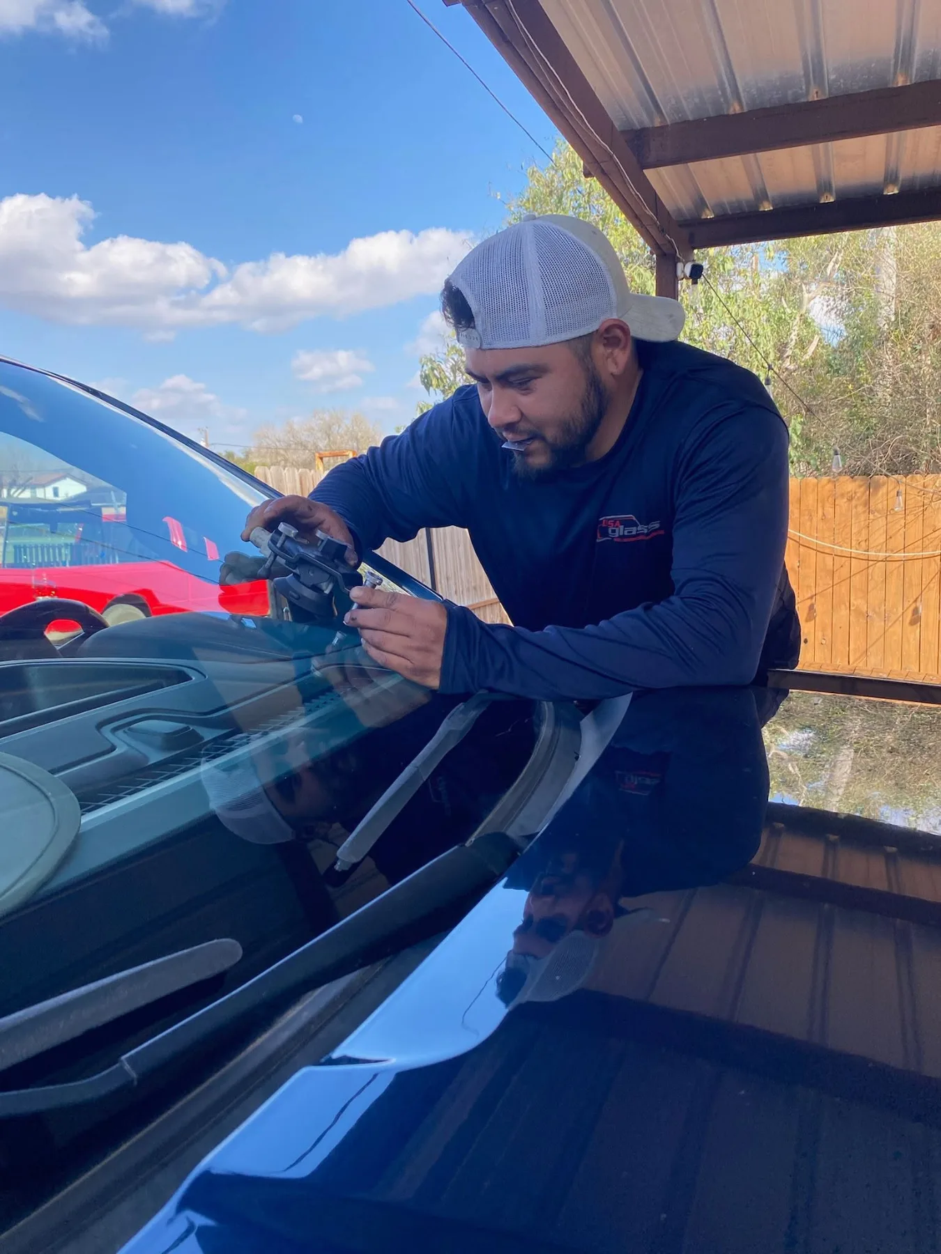 USA GLASS technician guiding a new windshield into place on a vehicle under the shop canopy